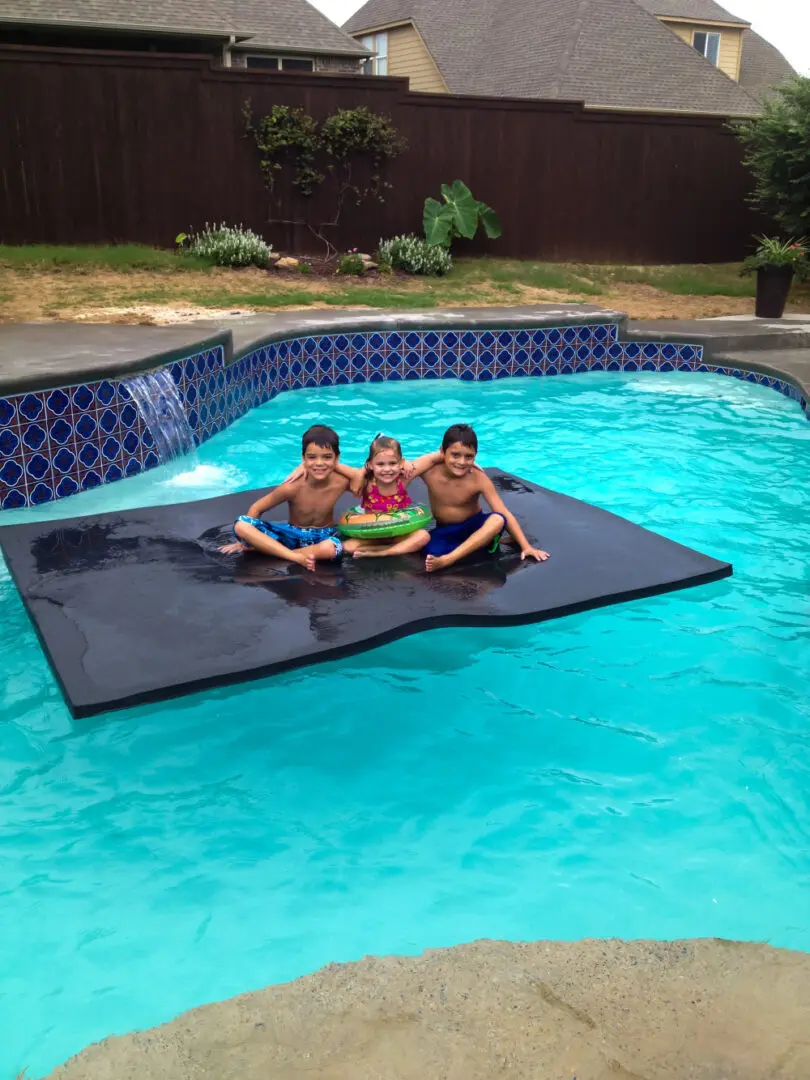 Kids on a black floating mat on a pool