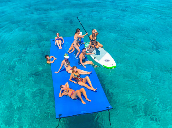Group of women playing on top of a floating water mat in clear ocean water