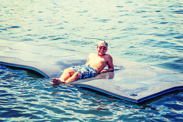 Guy leaning back on floating mat wearing a hat